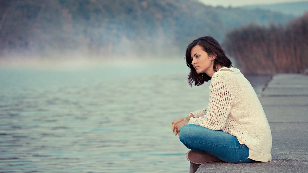 Young woman sitting by lake in the early morning.