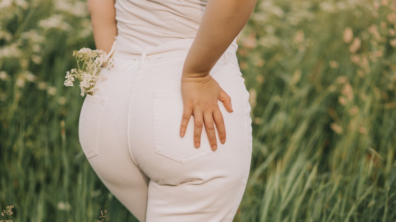 Closeup of a woman in white jeans on a blooming field background. Stylish look, fashion for curvy women, outdoor recreation.
