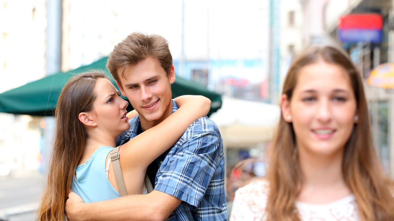 Unfaithful man hugging his girlfriend while is looking another one in the street