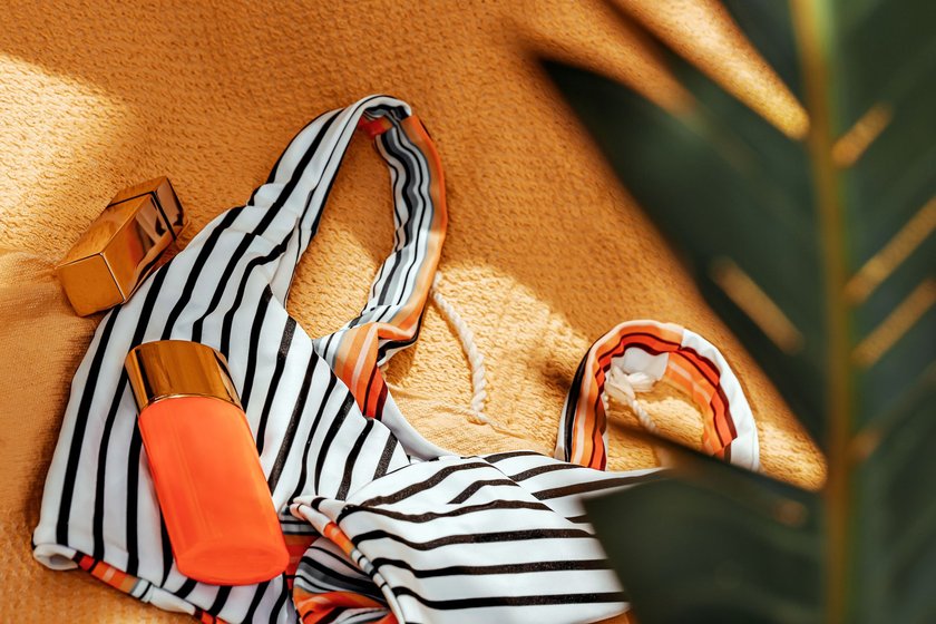 Closeup photo of beautiful beach items on the towel, stylish women's swimsuit with sunscreen and perfume as beach still life. Summer holidays concept. Vacation