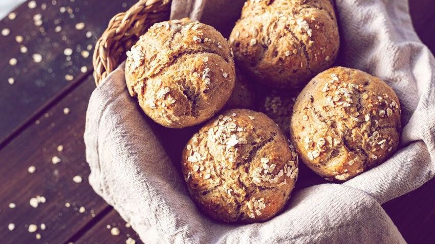 Breakfast rolls in a bread basket on wooden plank. Part of a series.