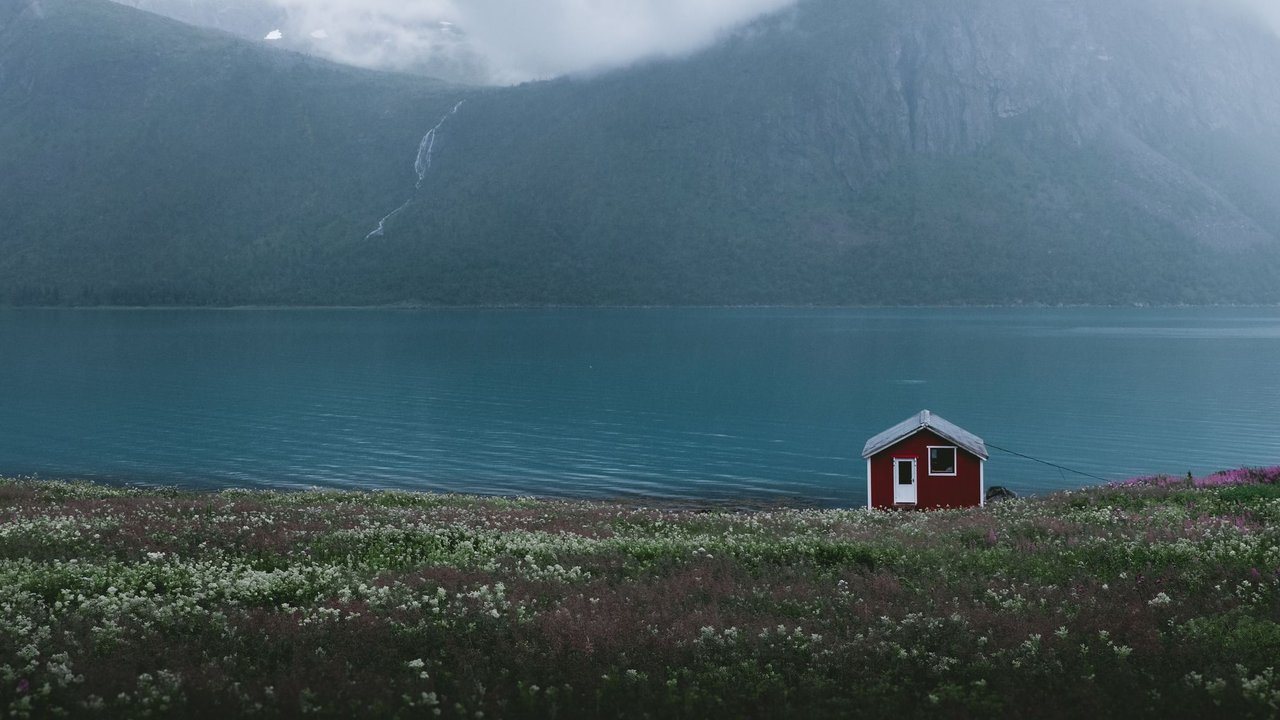 Ein einsames rotes Haus steht an an einem nebligen Fjord