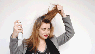 Frau sprüht sich Trockenshampoo auf den Haaransatz