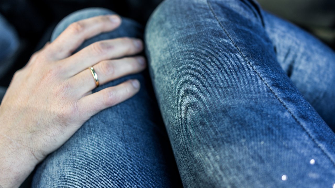 Man's hand with wedding ring on woman's legs in jeans in car