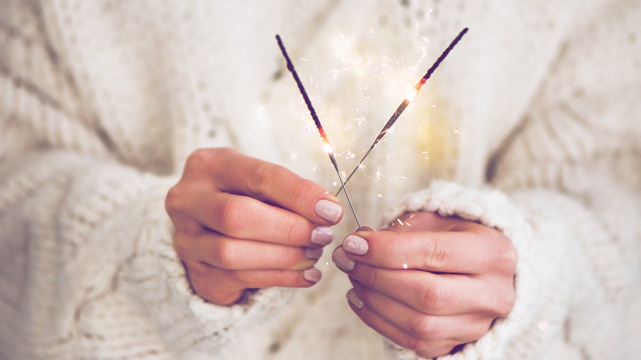Christmas or New Year celebration concept. Woman in white woolen sweater holding traditional festive sparklers in hands, close-up, square crop