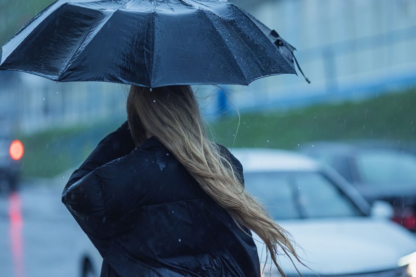 Eine Frau gerät in einen Regenschauer und hält einen Schirm