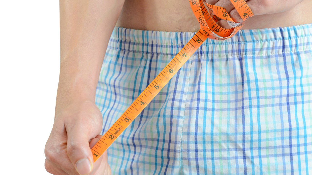 Young man holding tape measure, measuring his penis
