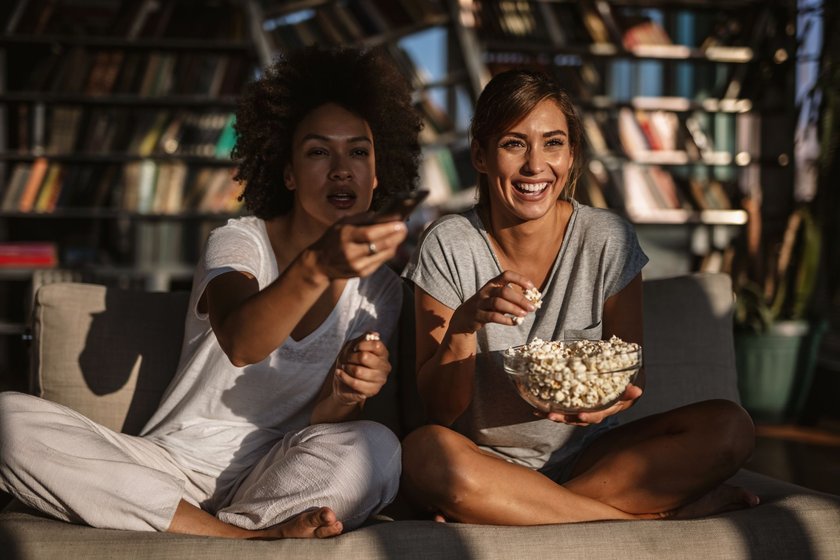 Female friends eating popcorn and watching a movie in the living room
