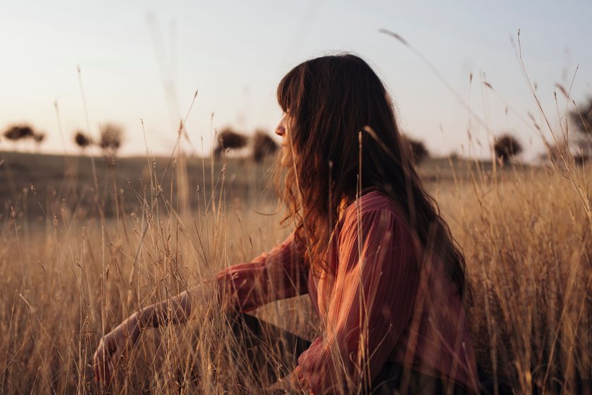 Profile shot of a beautiful young Caucasian woman looking away while enjoying the sunlight sitting in tall grass.