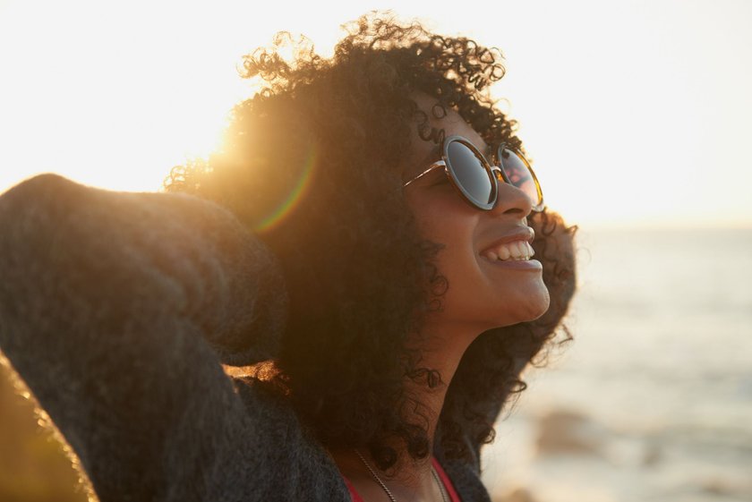 Eine Frau am Strand mit Sonnenbrille lächelt glücklich