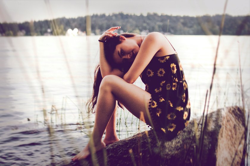 Frau, die im Sommerkleid am See sitzt