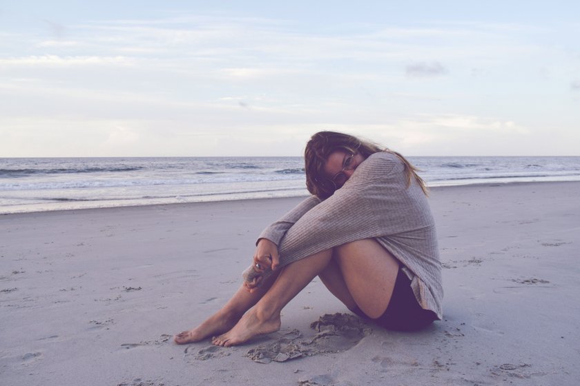 Frau, die am Strand sitzt und ihre Beine umfasst
