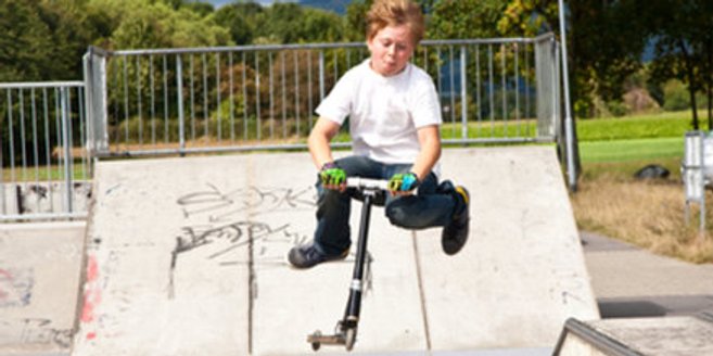 Kind mit Cityroller auf einer Halfpipe Kind mit Cityroller auf einer Halfpipe