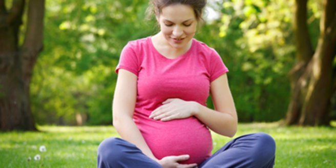 8. Schwangerschaftsmonat: Schwangere Frau sitzt auf Wiese und streichelt ihren Babybauch