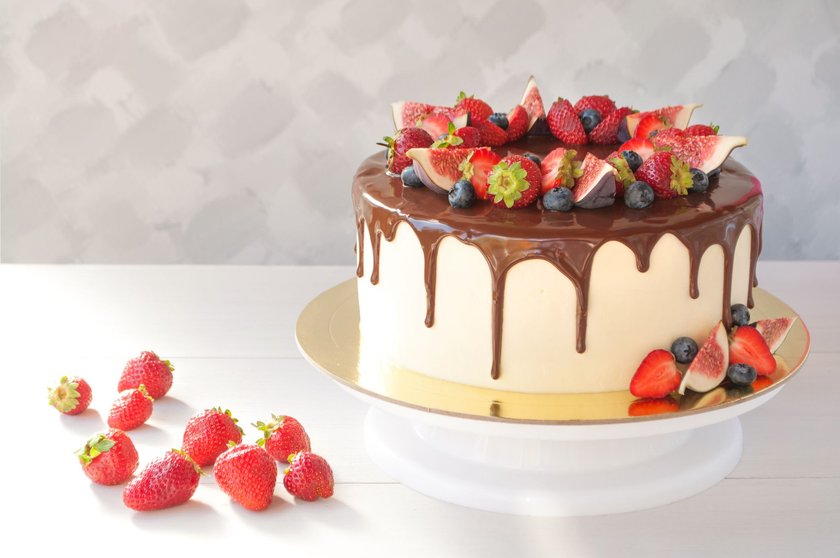 Cake in chocolate, decorated with slices strawberries, blueberries and figs on a white wooden table in the morning sun. Picture for a menu or a confectionery catalog.