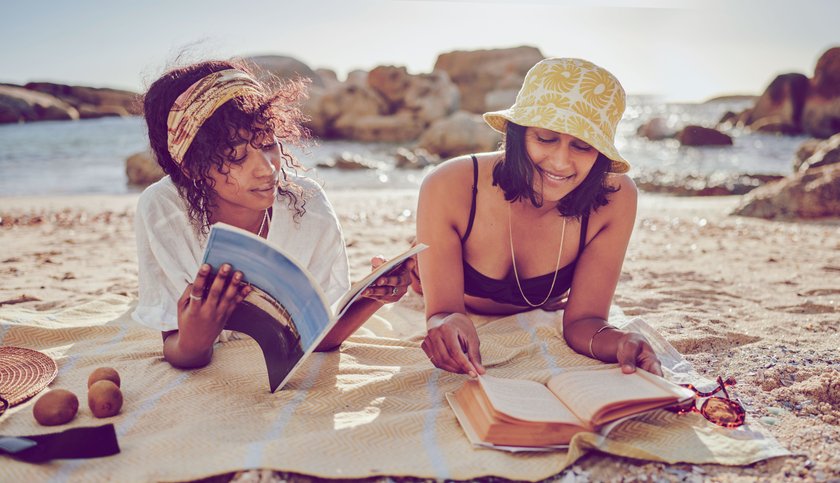 Zwei Frauen liegen am Strand und lesen