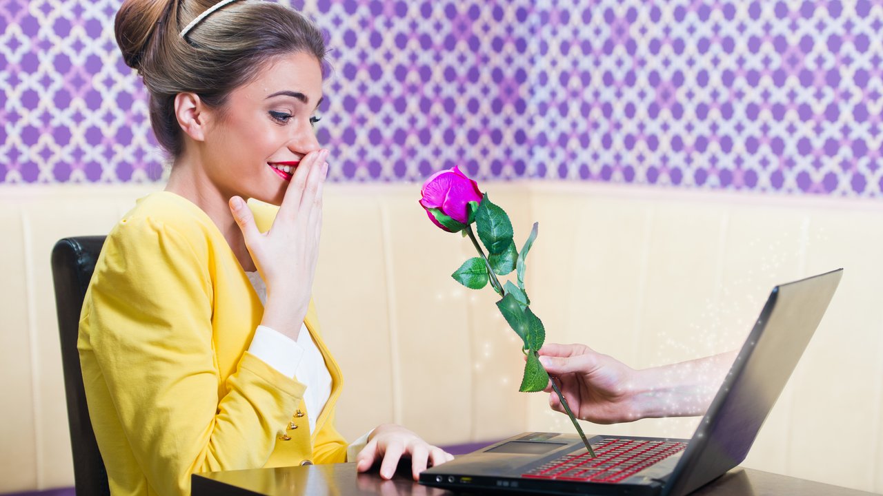 Man offering a rose to a beautiful woman over laptop screen