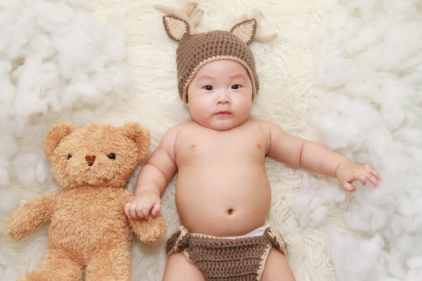 Baby liegt mit Windel, Mütze und Teddybär auf einer Decke