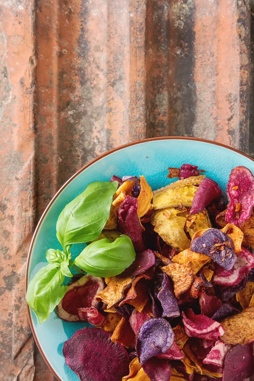 Beet and carrot salty chips in an old blue plate. Stone background.