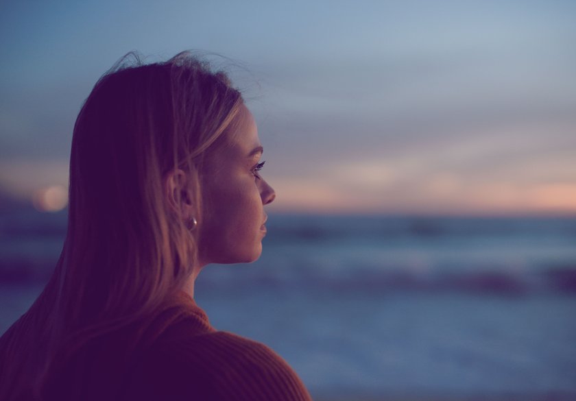 Frau schaut mit nachdenklichem Blick aufs Meer
