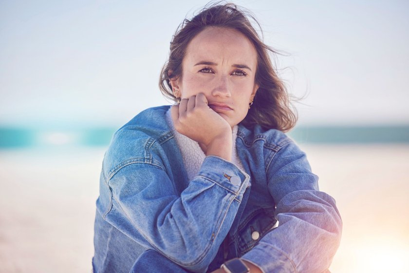 Frau, die traurig am Strand sitzt