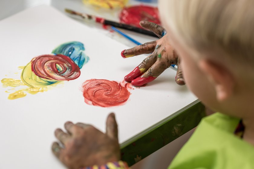 Kind sitzt am Tisch und malt mit Fingermalfarbe