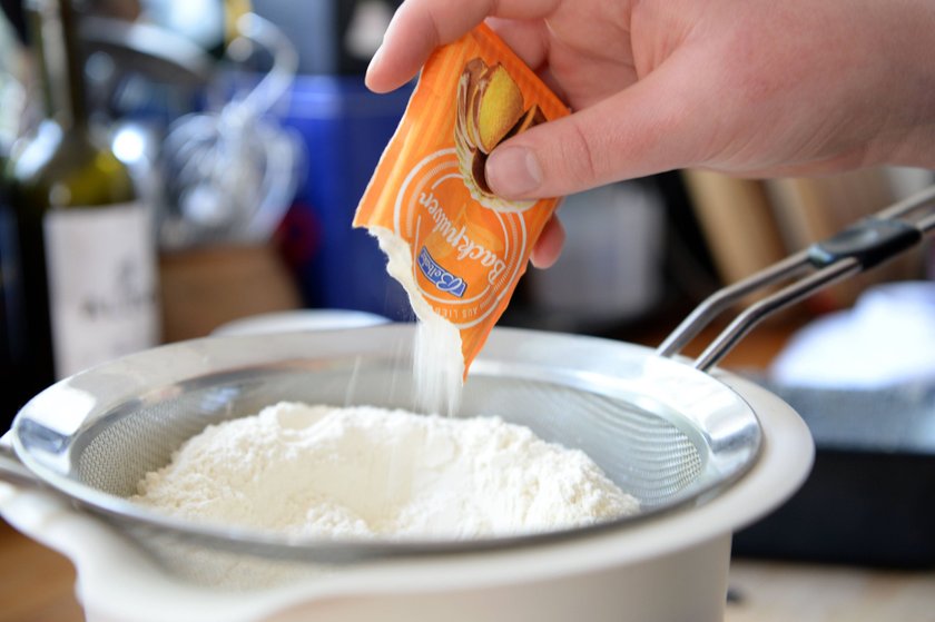 Symbolbild zum Thema Kuchen backen: Backpulver wird zum Mehl in einem Sieb in einer Rührschüssel gegeben 