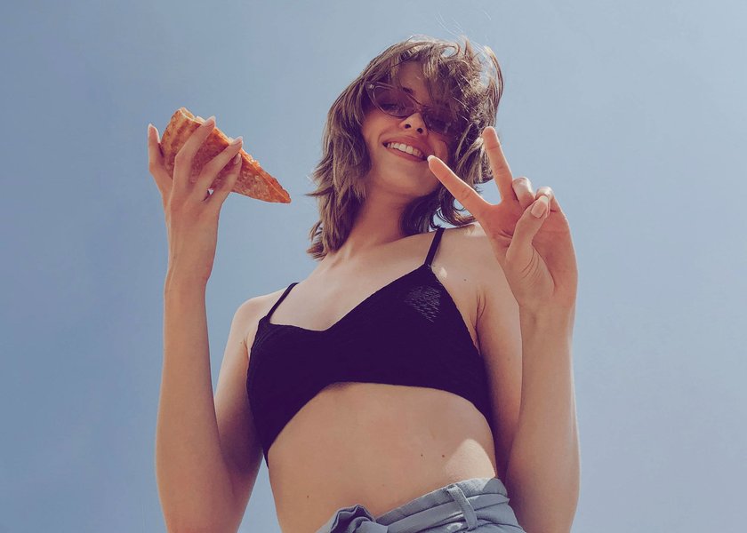 Frau mit Pizza in der Hand, die Peace-Zeichen macht