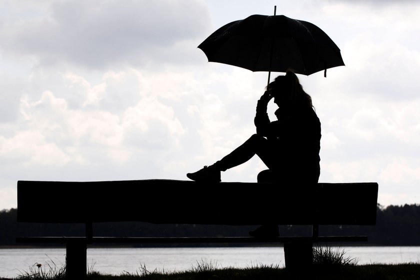 Frau sitzt unter einem Regenschirm an einem See auf einer Bank