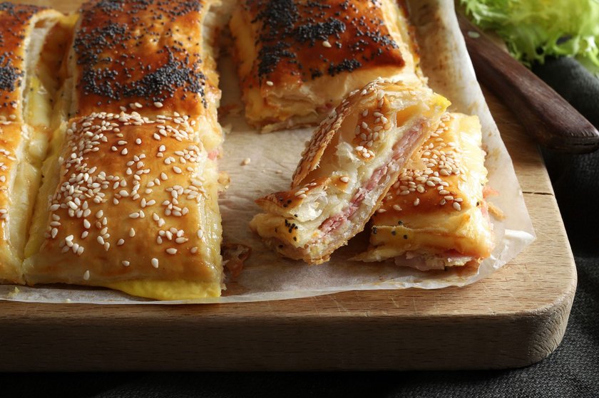 Rustic puff pastry filled with ham and cheese on a wooden cutting board. Directly above.