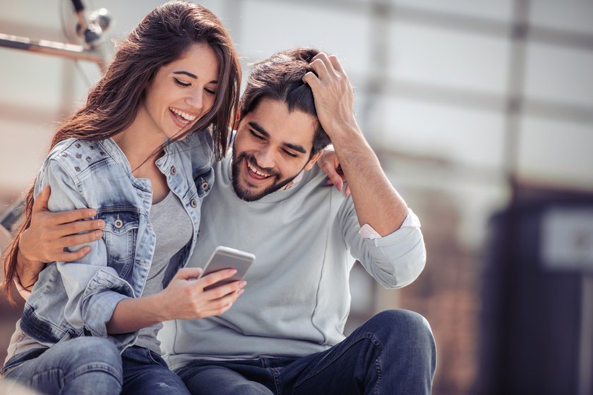 Frau und Mann schauen auf Handy und lachen