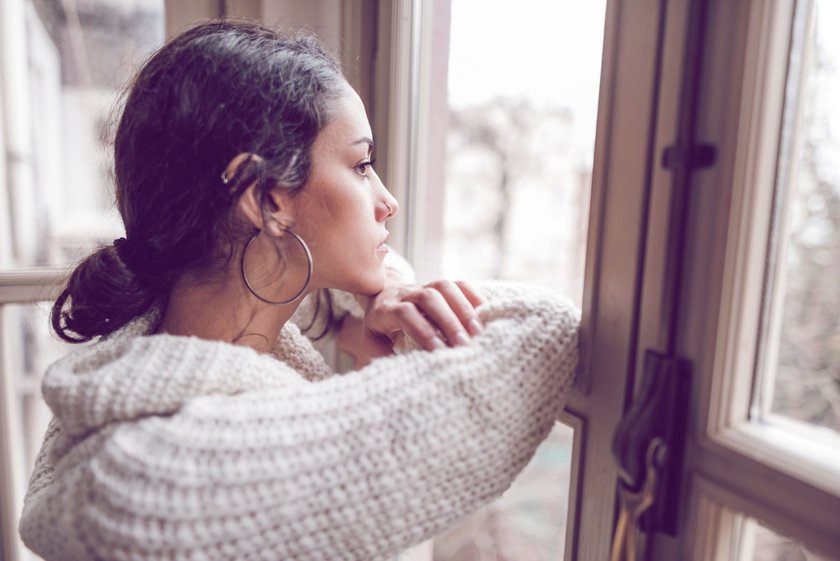 Frau mit nachdenklichem Blick schaut aus dem Fenster