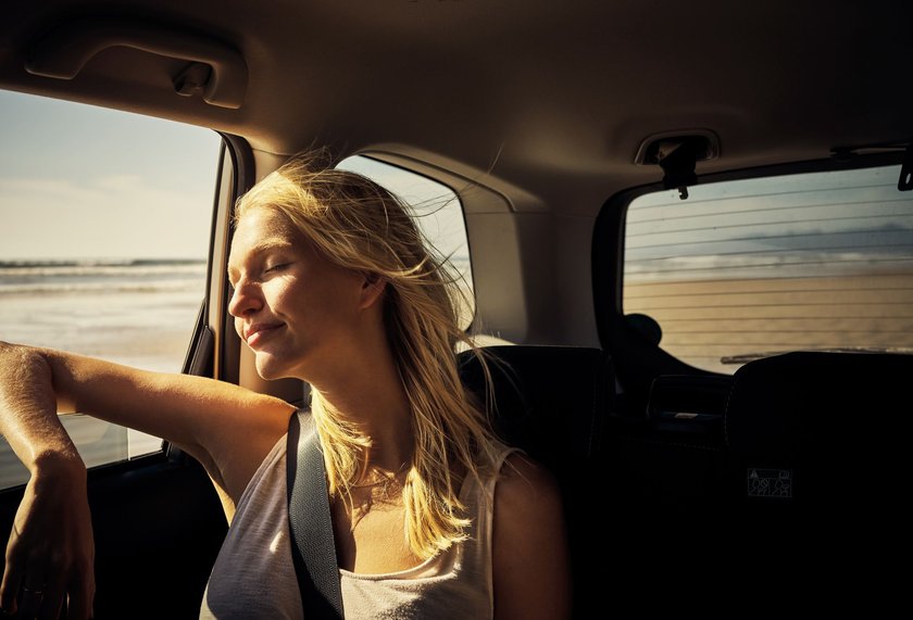 Eine Frau ist auf einem Roadtrip und sitzt hinten im Auto und genießt es