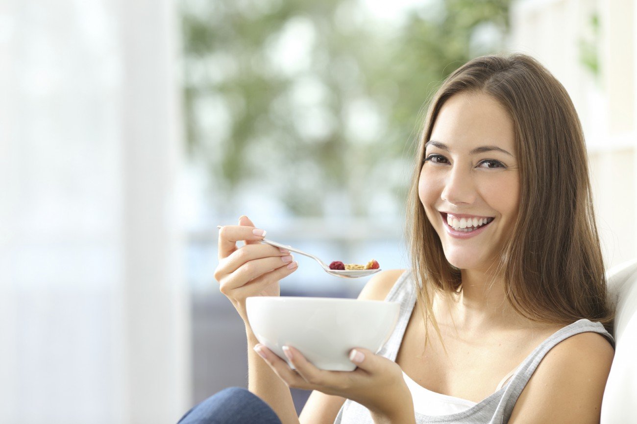 Casual happy woman dieting and eating cornflakes sitting on a couch at home Casual happy woman dieting and eating cornflakes sitting on a couch at home