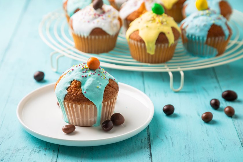 Easter or birthday cupcakes glazed with colorful sugar, sprinkles and chocolate for a kids party on a wooden turquoise table