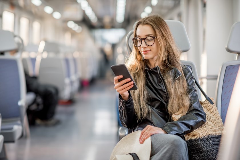 Frau sitzt im Zug und tippt am Handy