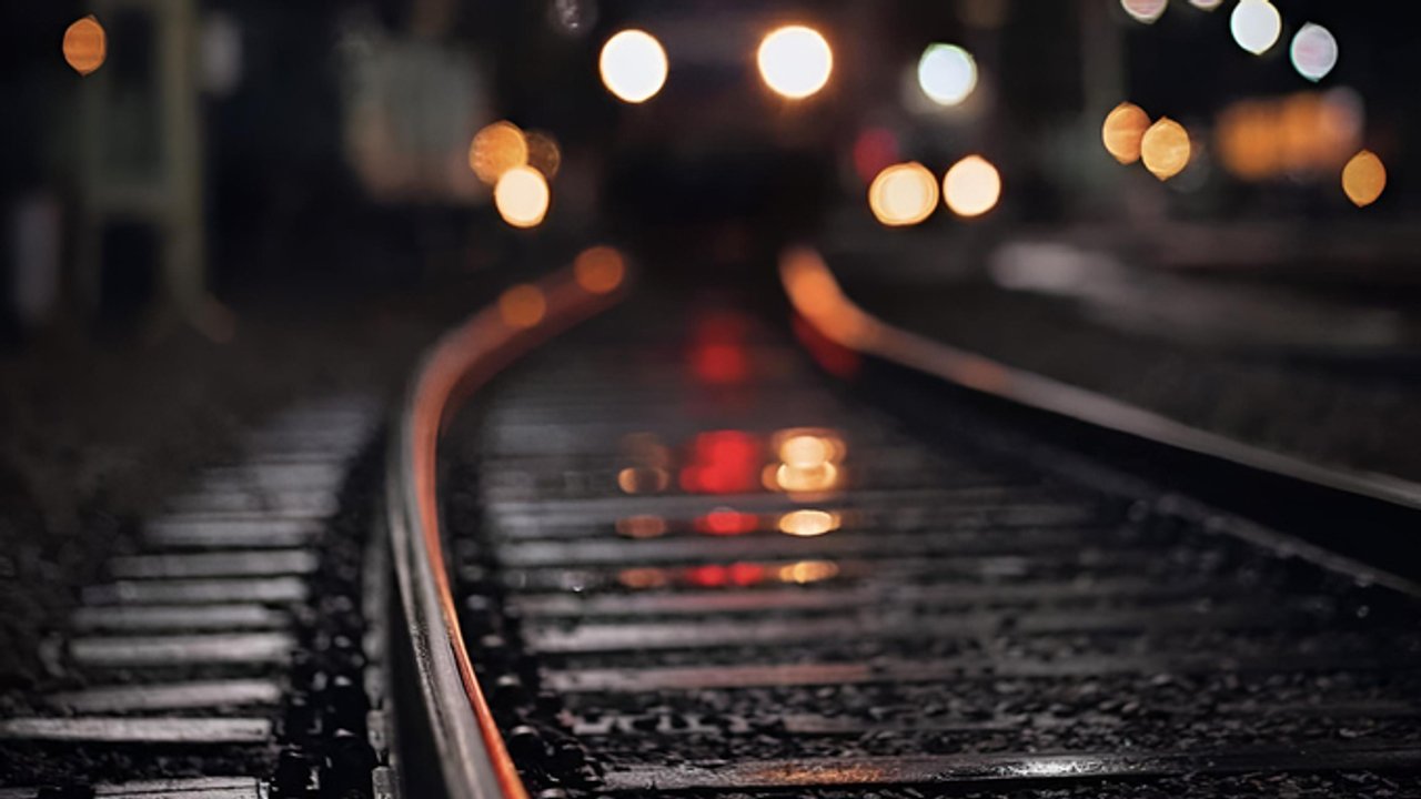 A close-up of a train moving along a set of tracks on a damp, dark night