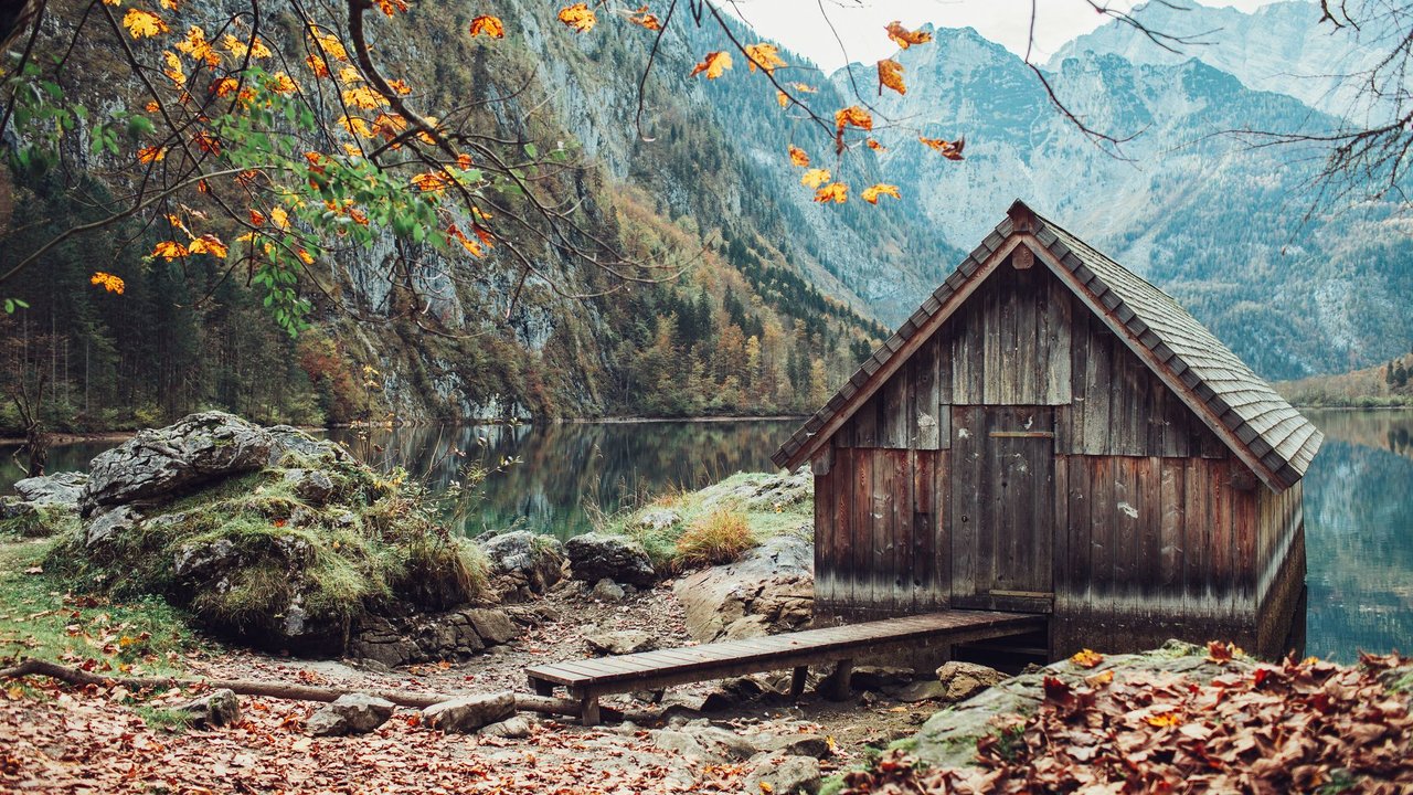 Eine einsame Hütte am See im Herbst mit Bergen im Hintergrund