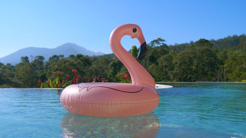 The hottest summer swimming accessory is the pink flamingo. An inflatable toy floats in a private pool in clear clear water in a tropical villa. The concept of vacation in an exotic country.