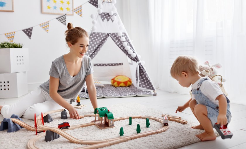 Mutter und Kind spielen im Kinderzimmer mit einer Holzeisenbahn