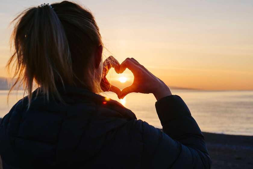 Frau macht Herzzeichen am Strand