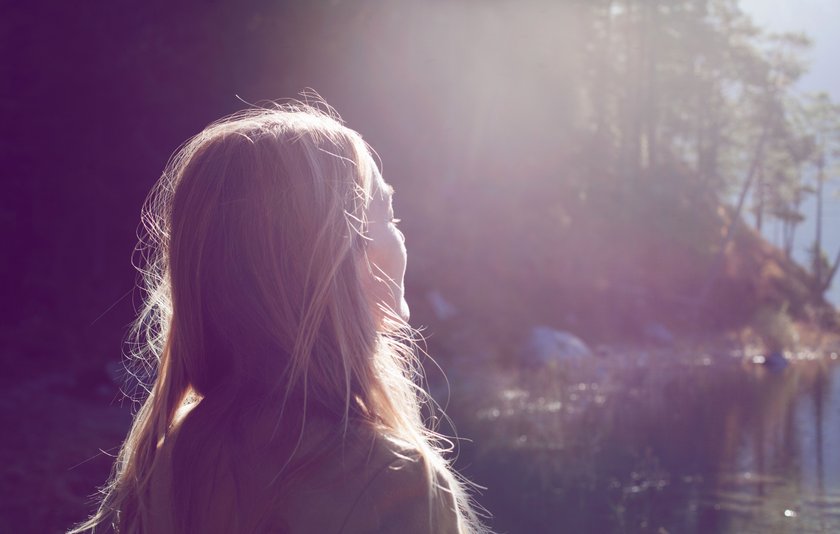 Frau im Wald, die der Sonne entgegenblickt