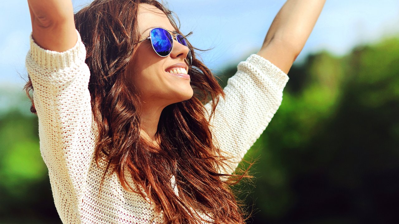 Attractive happy woman in sunglasses enjoying freedom outdoors with hand raised