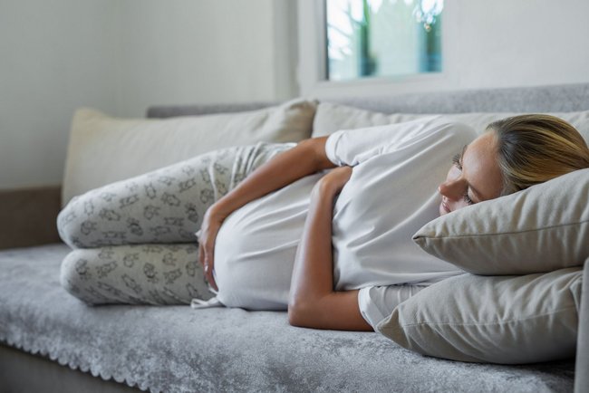 Seitenstechen in der Schwangerschaft: Schwangere liegt auf der Seite und hält sich den Bauch