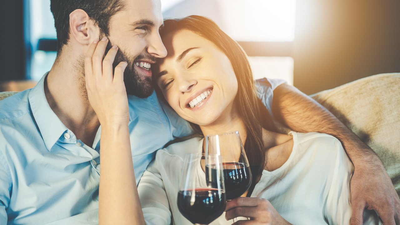 Beautiful young loving couple sitting close to each other and drinking red wine