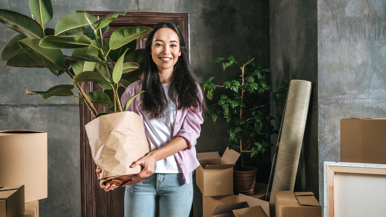 happy young woman with ficus plant and boxes moving into new house
